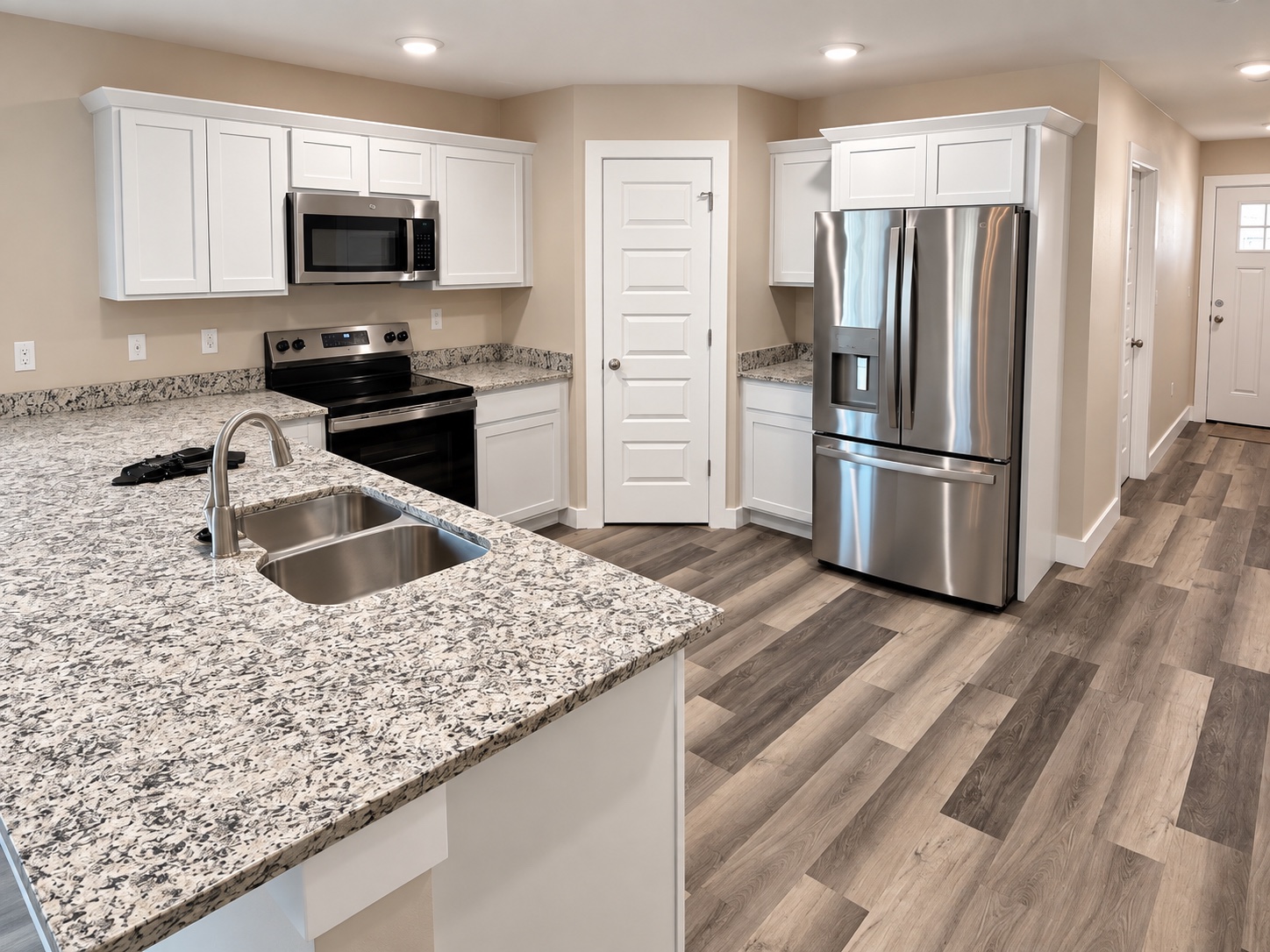 Wood-look flooring flowing through a kitchen and hallway, with white door trim and baseboards